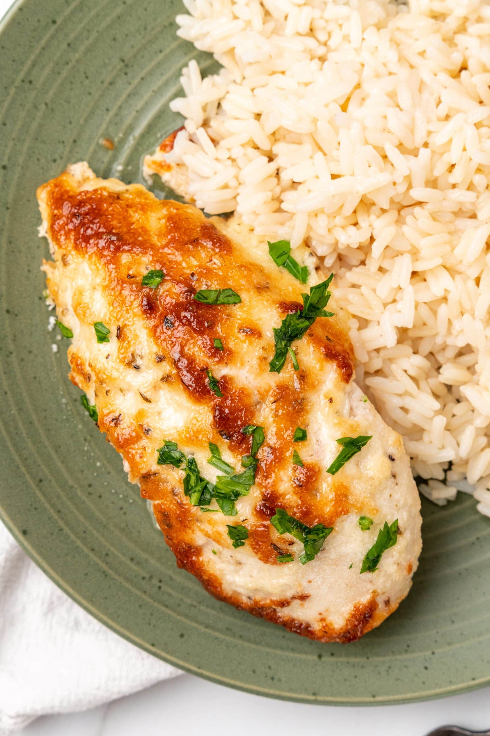a slice of mayo parmesan chicken on a green plate with cooked rice on the side