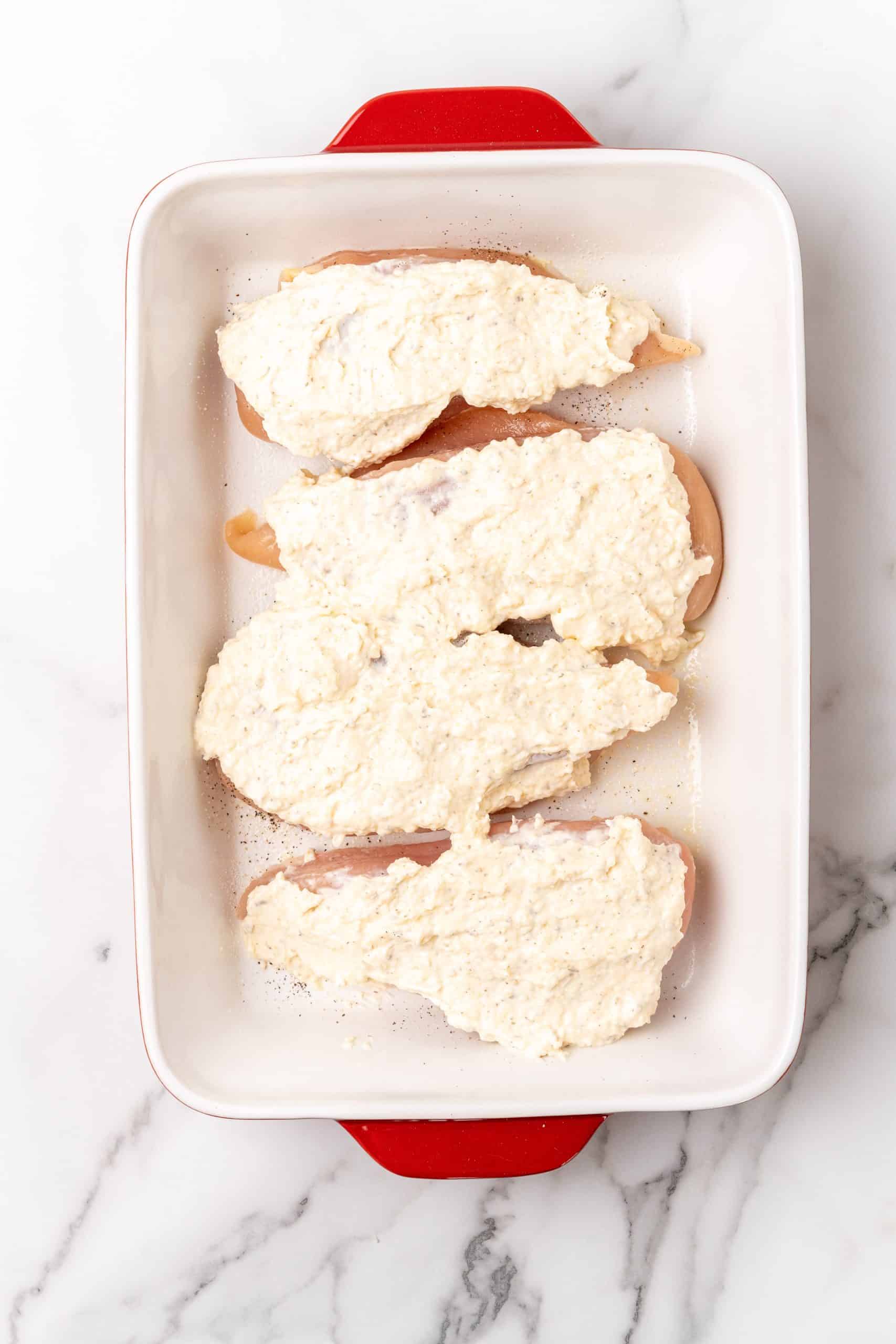 chicken breasts covered with a creamy cheese mayo mixture in a white baking dish