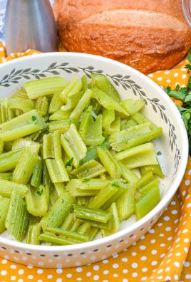 cooked braised celery shown in a white serving bowl with fresh bread and herbs in the back ground