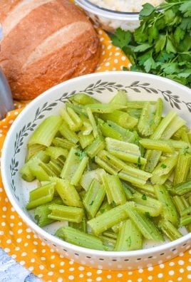 cooked braised celery shown in a white serving bowl with fresh bread and herbs in the back ground