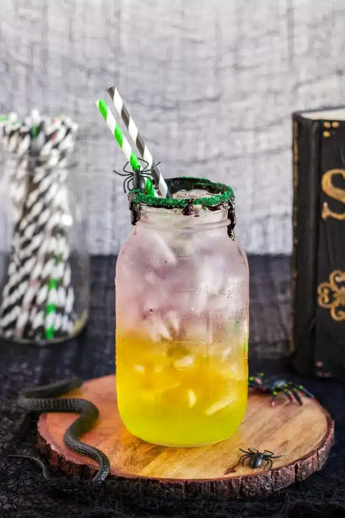 a layered halloween drink in a glass jar sitting on a wooden cutting board