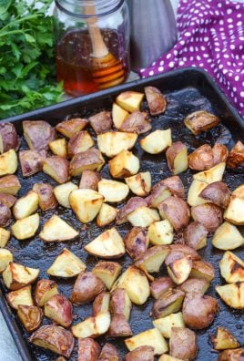 honey roasted red potatoes on a dark brown sheet pan with a brunch of fresh parsley and a jar of honey in the background
