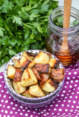 honey roasted red potatoes shown in a purple bowl with fresh herbs and a jar of honey in the background