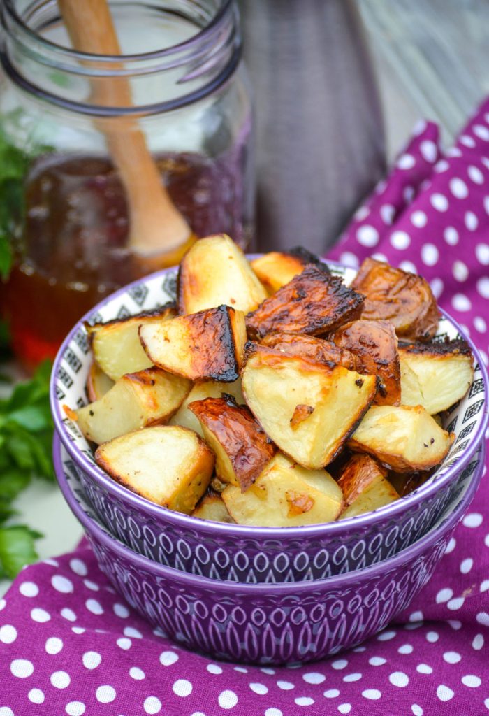 honey roasted red potatoes shown in a purple bowl with fresh herbs and a jar of honey in the background