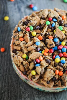 a monster cheese cake release from it's springform pan & topped with crushed chocolate chip cookies and miniature m&m's