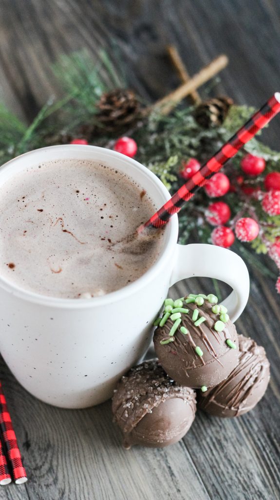 a mug of warm cocoa made from homemade hot cocoa bombs shown at the base of the cup with Christmas greenery in the background