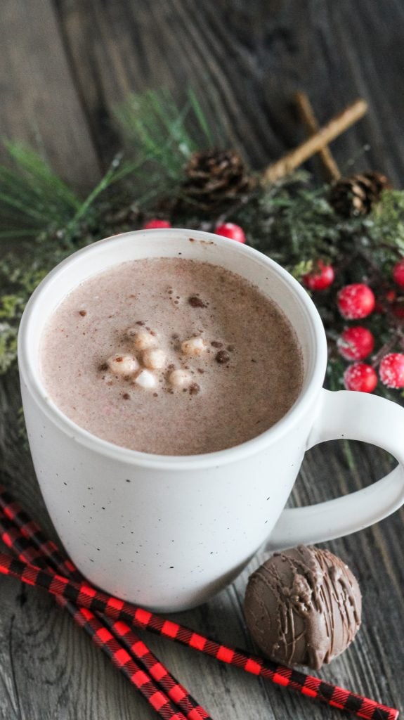 a mug of warm cocoa made from homemade hot cocoa bombs shown at the base of the cup with Christmas greenery in the background