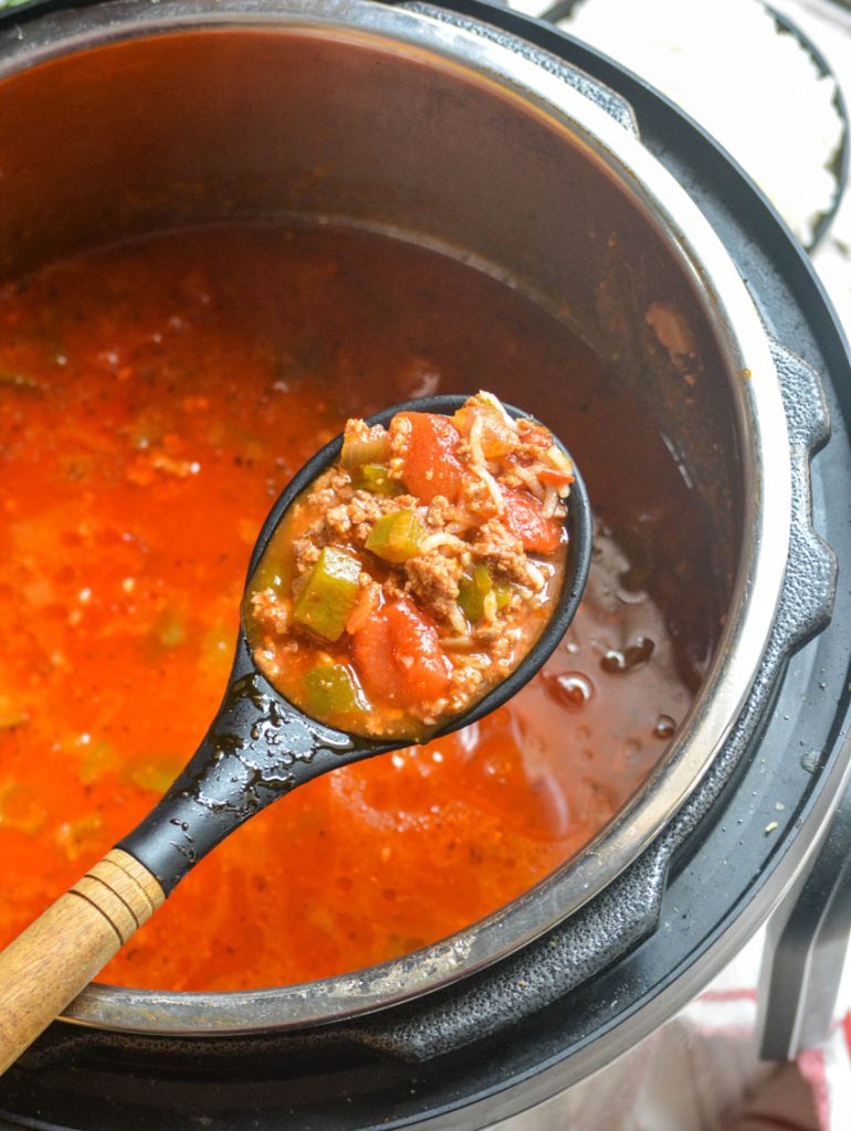 a spoon shown holding aloft a scoop of stuffed pepper soup above the bowl of an Instant Pot