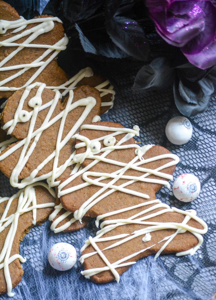a stack of mummy decorated gingerbread cookies with candy eye balls and spiders web in the back ground