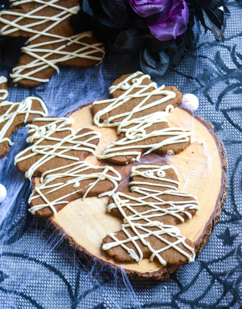 Halloween themed mummy gingerbread cookies on a wooden cutting board with spider webs in the background