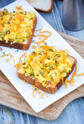 open faced Denver omelet sandwiches on a white platter topped with melted cheddar and a drizzle of hot sauce