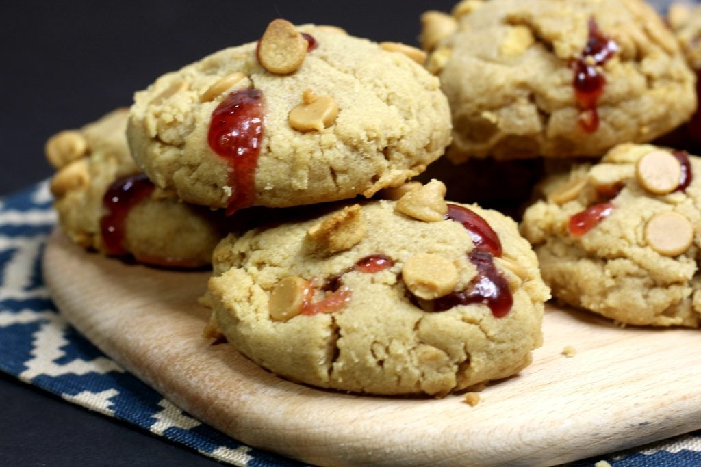 peanut butter and stuffed jelly cookies piled on a wooden cutting board