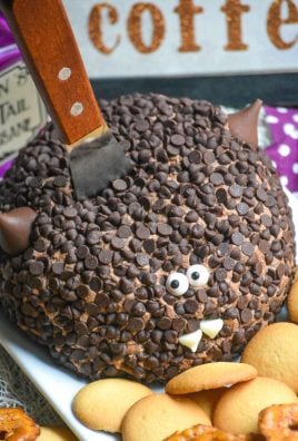 a triple chocolate dessert cheese ball covered in mini chocolate chips and made to look like a bat with a wooden handled spread stuck in the middle