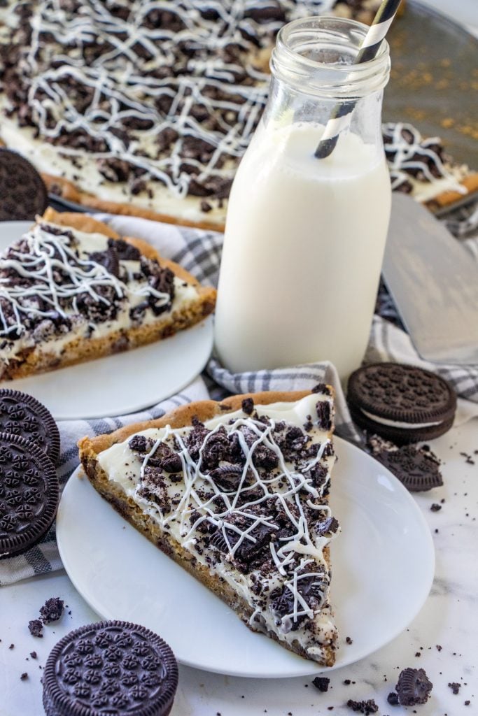 slices of cookies and cream dessert pizza served on white dessert plates with a glass of milk in the background