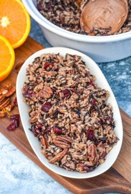 cranberry pecan wild rice stuffing shown on a small white platter on a wooden cutting board with fresh fruit and nuts