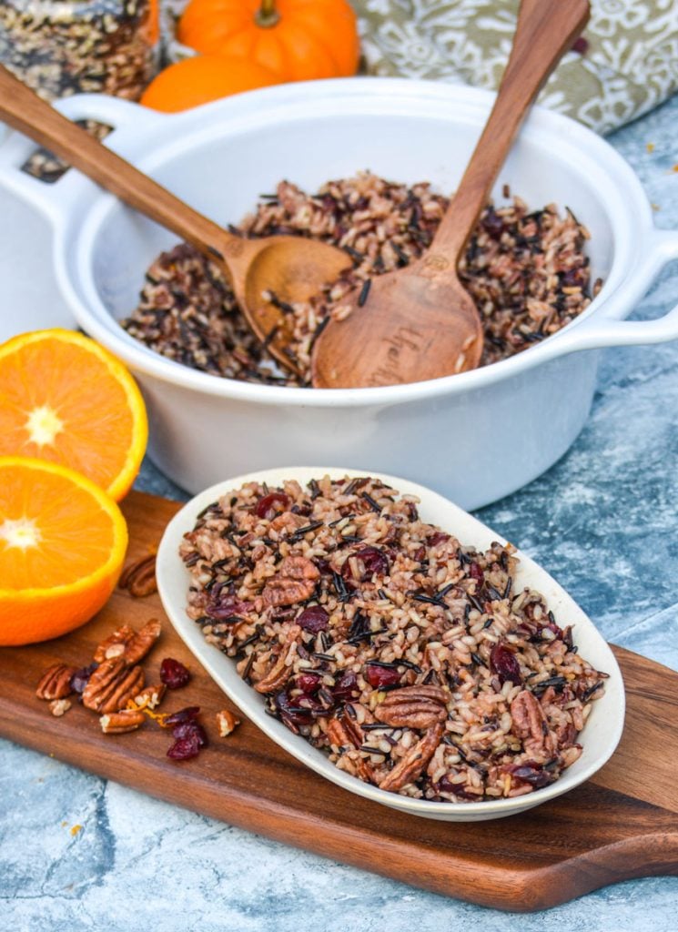 cranberry pecan wild rice stuffing shown on a small white platter on a wooden cutting board with fresh fruit and nuts 