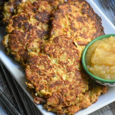 crispy mashed potato & stuffing pancakes shown on a white platter with a small bowl of applesauce on the side
