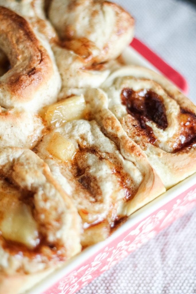 caramel apple cinnamon rolls shown baked in a red square baking dish