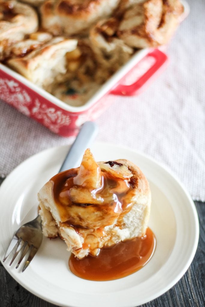 a caramel apple cinnamon rolls served on a white plate and drizzled with extra caramel sauce