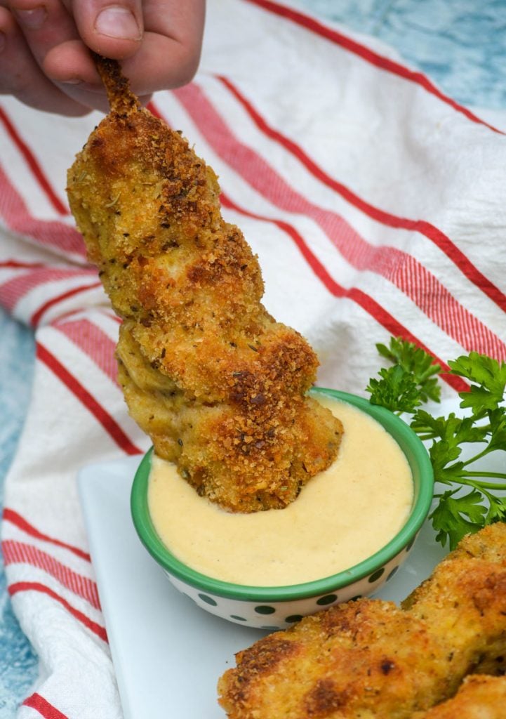 a small hand shown dipping a single city chicken skewer into a small green bowl of honey mustard