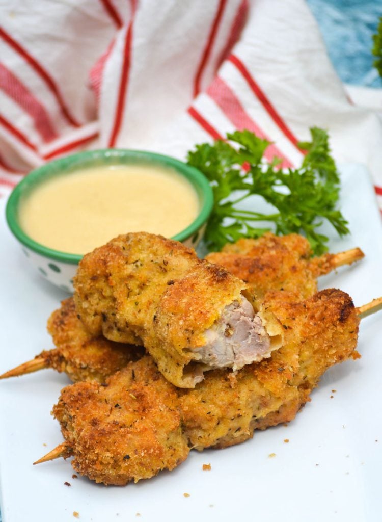 three skewers of Nonna's fried city chicken on a white platter served with fresh herbs and honey mustard sauce for dipping