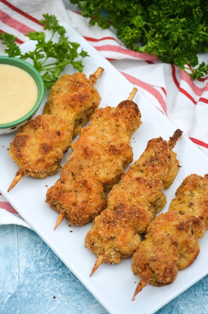 three skewers of Nonna's fried city chicken on a white platter served with fresh herbs and honey mustard sauce for dipping