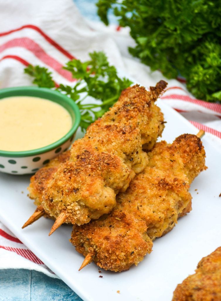 three skewers of Nonna's fried city chicken on a white platter served with fresh herbs and honey mustard sauce for dipping