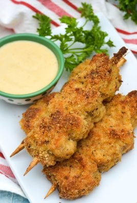 three skewers of Nonna's fried city chicken on a white platter served with fresh herbs and honey mustard sauce for dipping