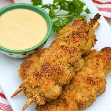 three skewers of Nonna's fried city chicken on a white platter served with fresh herbs and honey mustard sauce for dipping