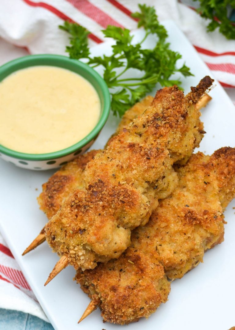 three skewers of Nonna's fried city chicken on a white platter served with fresh herbs and honey mustard sauce for dipping