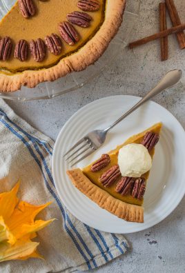 a slice of pumpkin pie with pecans served on a small white plate with silver forks for eating