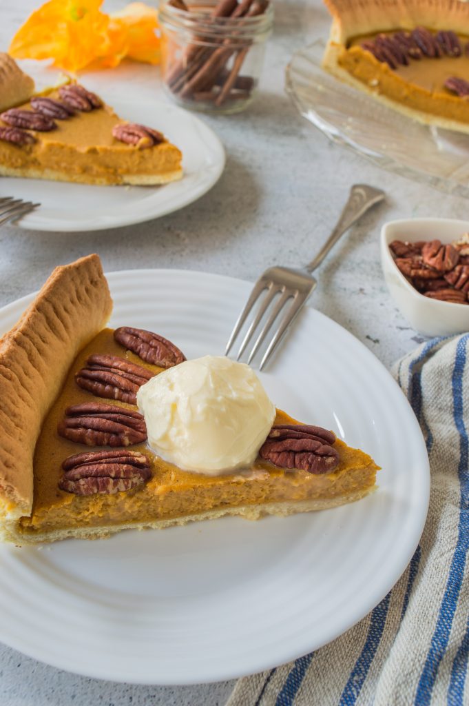 a slice of homemade pumpkin pie with pecans served on a small white plate with silver forks for eating