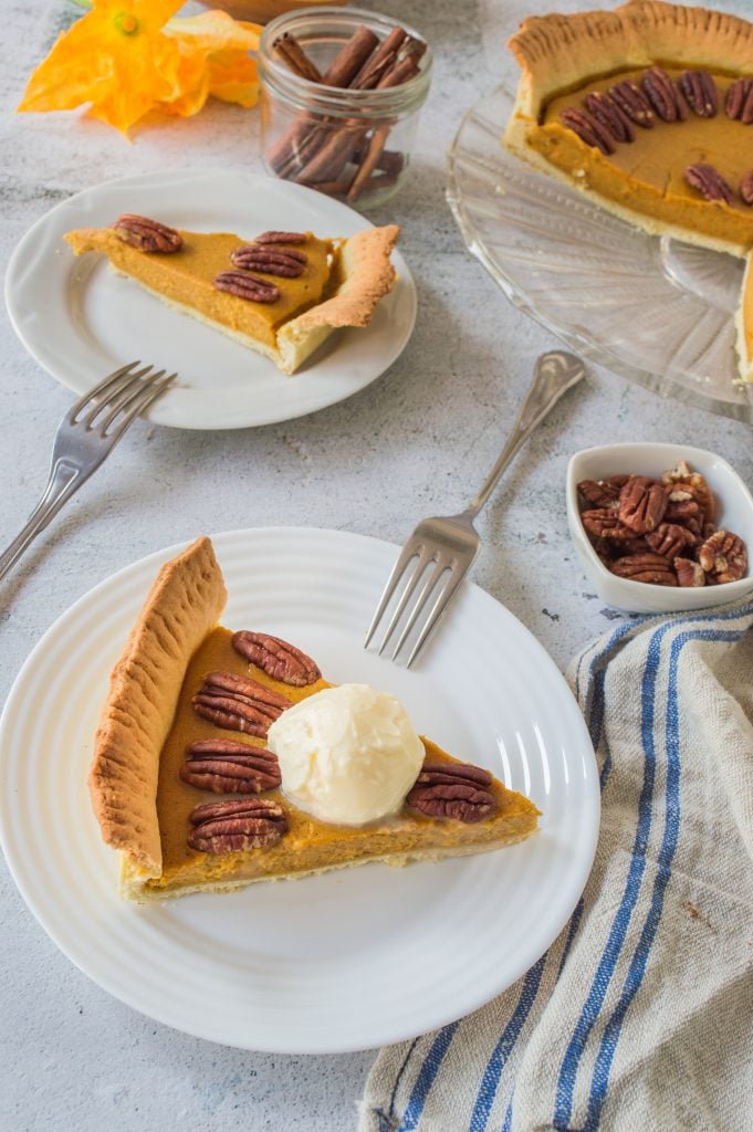 a slice of homemade pumpkin pie with pecans served on a small white plate with silver forks for eating
