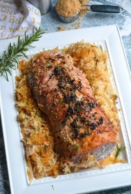 roasted pork loin with seasoned sauerkraut on a white serving platter with a sprig of fresh rosemary