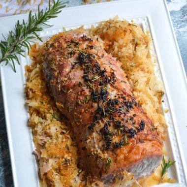 roasted pork loin with seasoned sauerkraut on a white serving platter with a sprig of fresh rosemary