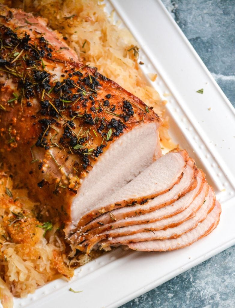 oven roasted pork loin with rosemary brown sugar sauerkraut shown on a white platter, surrounded by the sweetened cabbage and thinly sliced