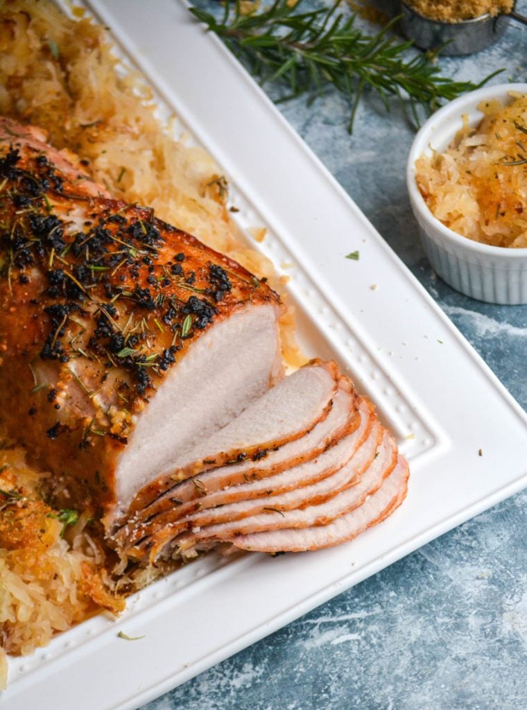 roasted pork loin with rosemary sauerkraut shown on a white platter, surrounded by the sweetened cabbage and thinly sliced