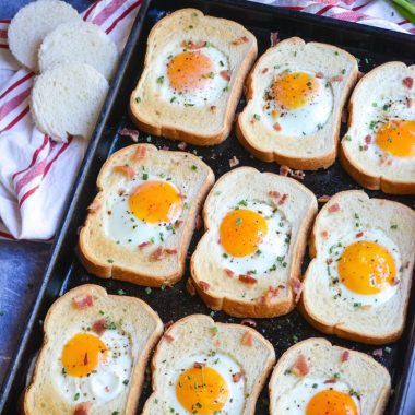 sheet pan egg in a hole shown on a dark brown sheet pan with a cloth napkin, cut out bread holes, and a bunch of green onions in the background
