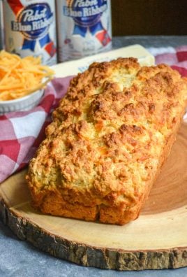 a loaf of cheesy beer bread shown on a wooden cutting board