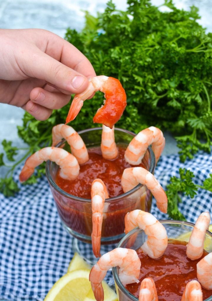 a hand holding aloft a steamed shrimp covered in cocktail sauce