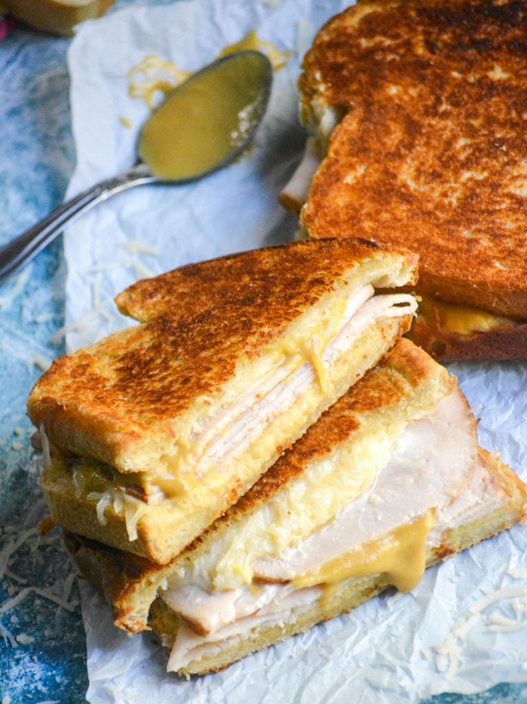 two halves of a crispy Dijon turkey melt sandwich stacked on top of each other to reveal layers of meat and melted cheese