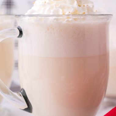 creamy white christmas punch shown in a glass jar, topped with whipped cream and golden sprinkles