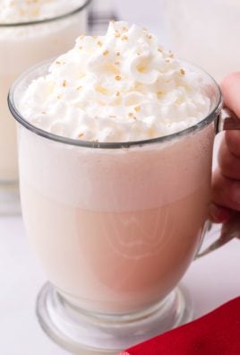 creamy white christmas punch shown in a glass jar, topped with whipped cream and golden sprinkles