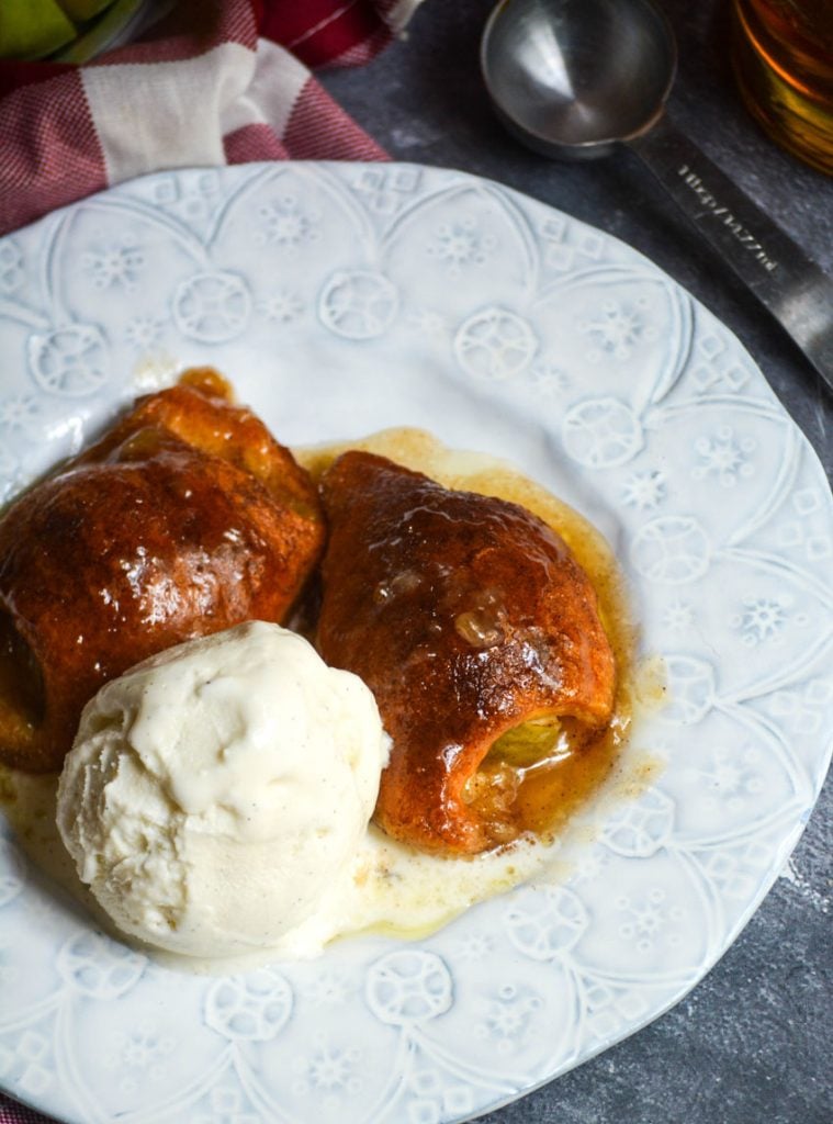 fireball whiskey glazed apple dumplings served on white plates with a scoop of vanilla ice cream