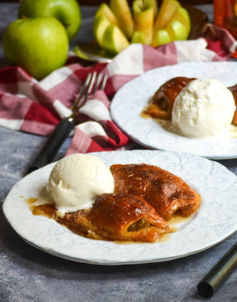 fireball whiskey glazed apple dumplings served on white plates with a scoop of vanilla ice cream