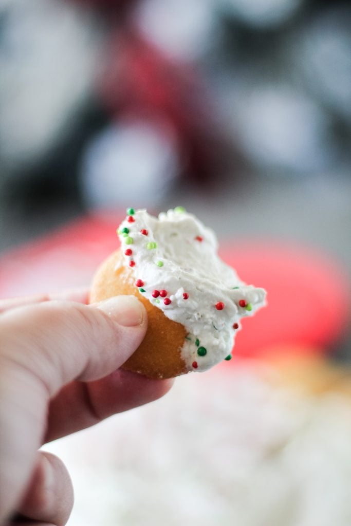 a hand holding up a vanilla wafer dunked in christmas tree cake dip