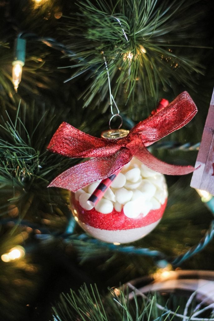 clear plastic ornaments filled with layers of hot cocoa mix, colored sprinkles, and mini marshmallows shown on a lit Christmas tree