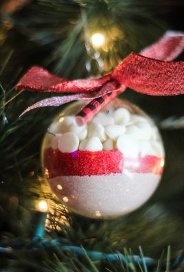 clear plastic ornaments filled with layers of hot cocoa mix, colored sprinkles, and mini marshmallows shown on a lit Christmas tree