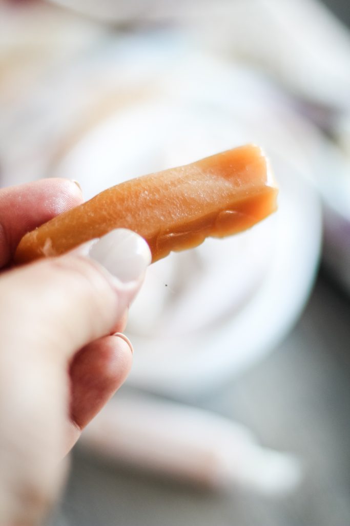 a hand holding up a chewy homemade caramel