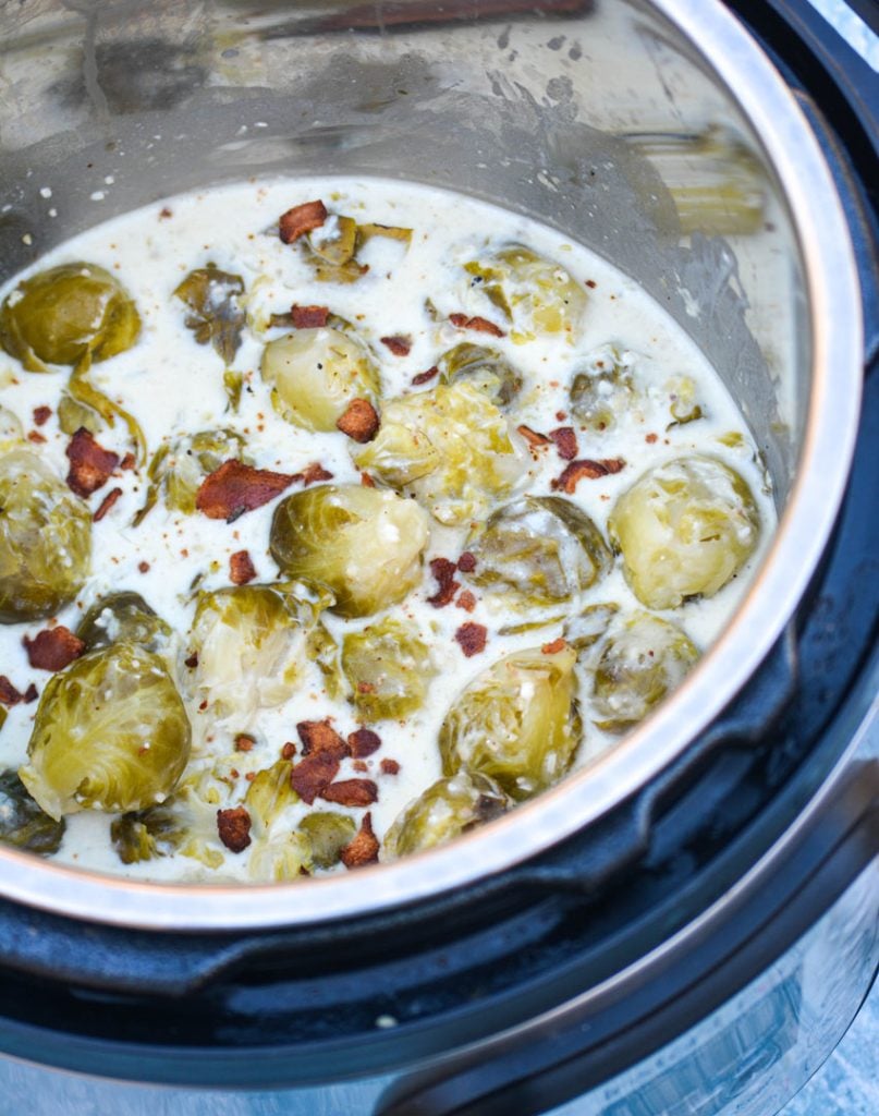 Instant Pot creamed brussels sprouts shown in the pot in a thick cream sauce and topped with crisp crumbled bacon